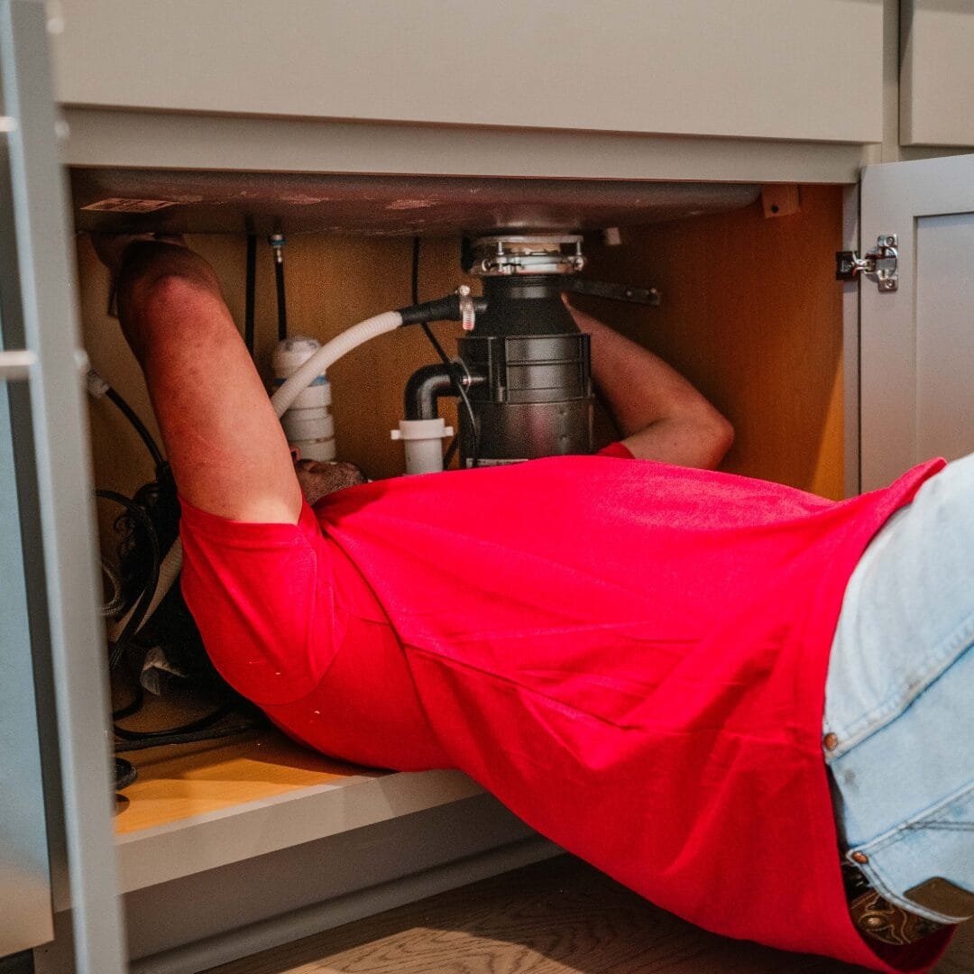 A member of the Todd's Plumbing team cleaning the drain under a kitchen sink.